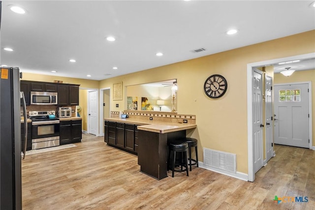 501 Hathaway St, Victoria, TX 77904 - kitchen featuring stainless steel appliances, a breakfast bar, decorative backsplash, light wood-style flooring, and light countertops