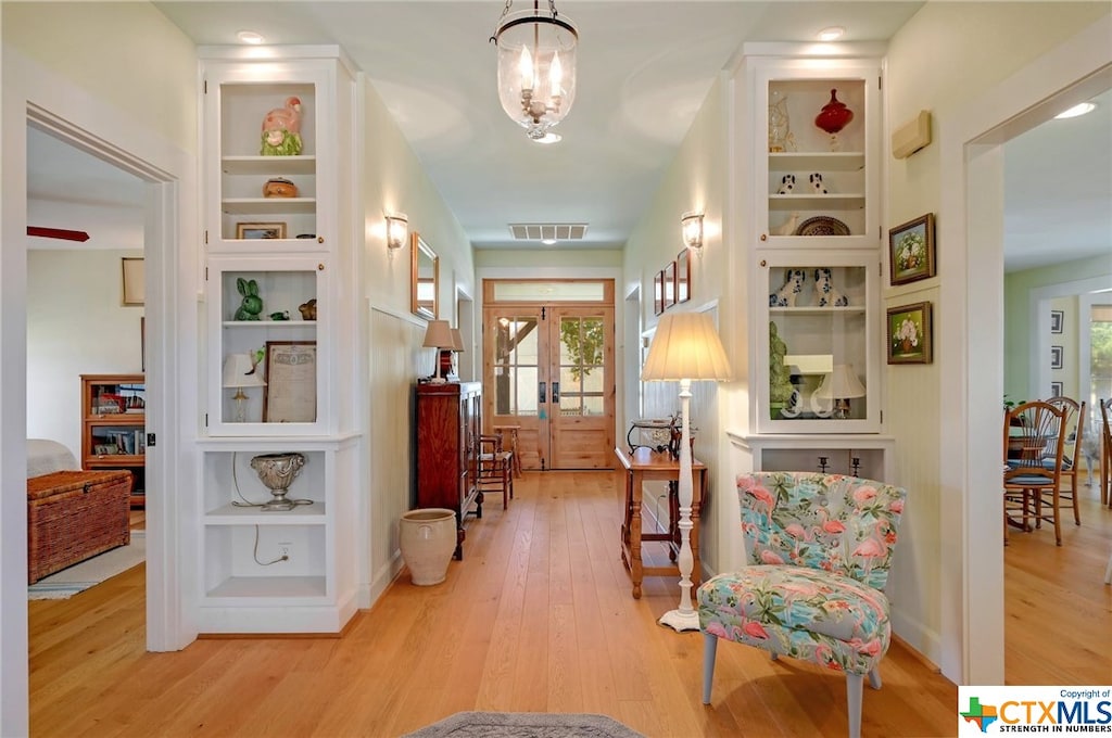 living area featuring a chandelier, plenty of natural light, light wood-type flooring, and french doors