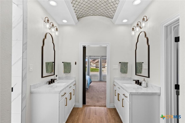 ensuite bathroom with a sink, baseboards, two vanities, and wood finished floors