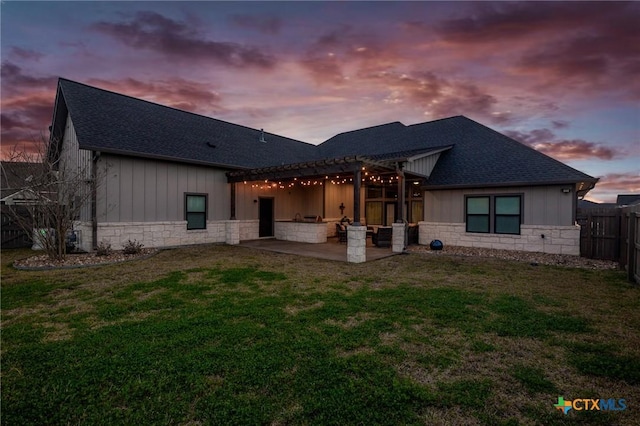 back of property at dusk with a yard, stone siding, and a patio