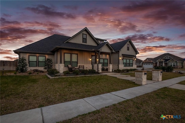 view of front of house featuring stone siding, a shingled roof, board and batten siding, and a yard