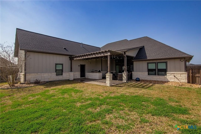 rear view of property with stone siding, a patio area, a lawn, and roof with shingles