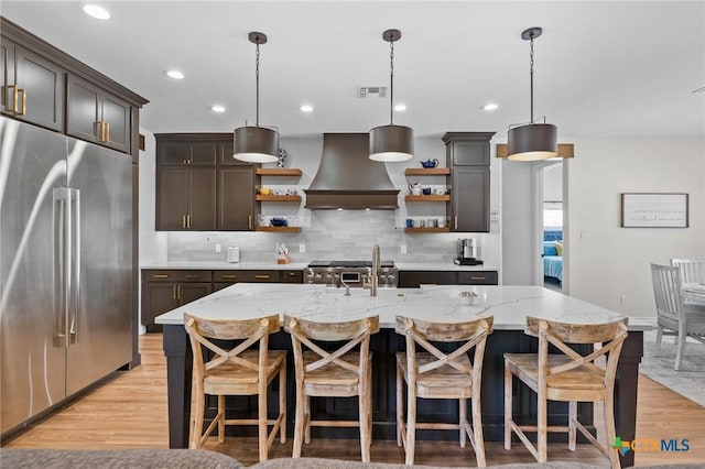 kitchen featuring light wood finished floors, appliances with stainless steel finishes, open shelves, tasteful backsplash, and custom range hood