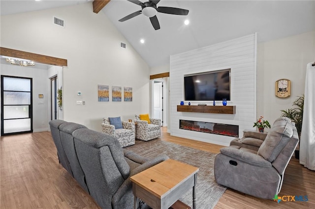 living area with visible vents, a glass covered fireplace, wood finished floors, high vaulted ceiling, and beam ceiling