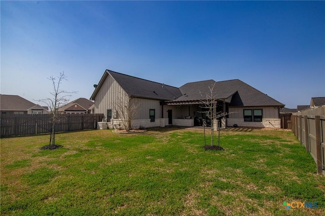 back of property featuring a yard, board and batten siding, stone siding, and a fenced backyard