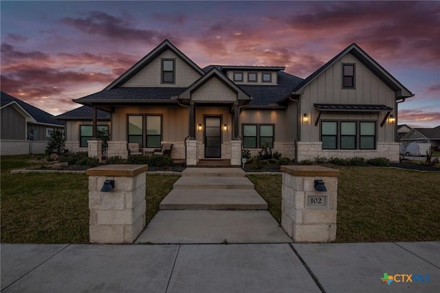 view of front facade with stone siding, board and batten siding, a front yard, and roof with shingles