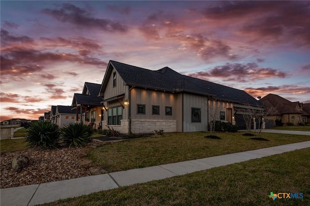 view of front of home with an attached garage, board and batten siding, a front yard, stone siding, and driveway