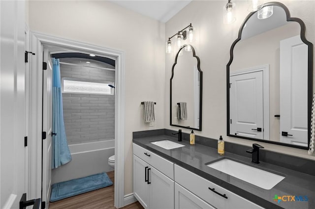 full bath featuring double vanity, wood finished floors, a sink, and toilet