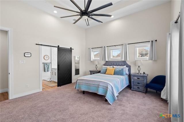 bedroom with a barn door, a high ceiling, carpet flooring, baseboards, and ensuite bath