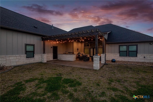 rear view of property featuring roof with shingles, stone siding, board and batten siding, and a patio