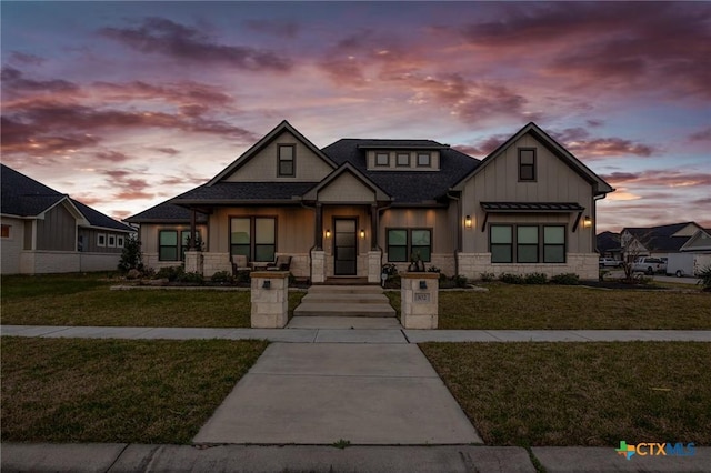 view of front of house featuring stone siding, a lawn, board and batten siding, and roof with shingles