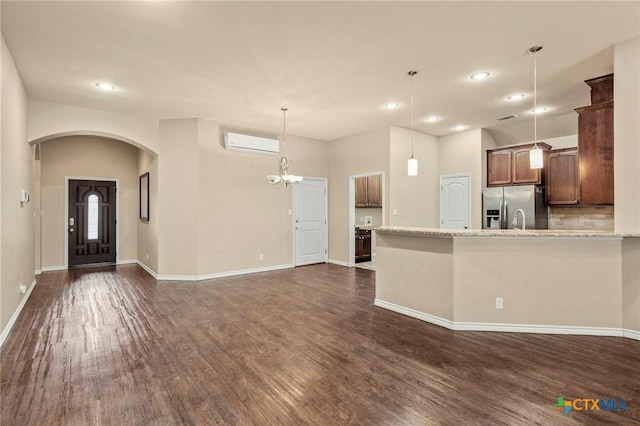 kitchen with a wall mounted air conditioner, stainless steel fridge, light stone counters, and pendant lighting