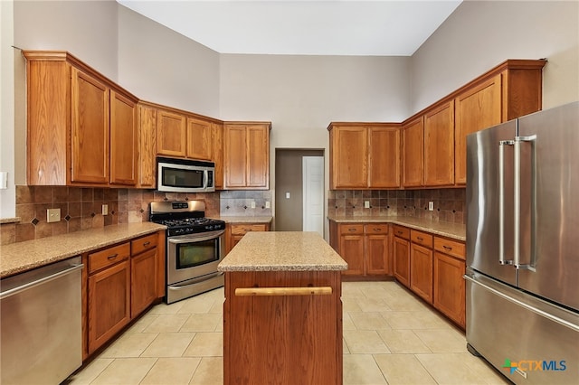 kitchen with brown cabinetry, appliances with stainless steel finishes, a center island, and tasteful backsplash