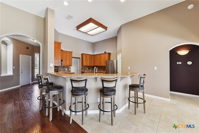 kitchen with brown cabinetry, high end refrigerator, decorative backsplash, a peninsula, and arched walkways