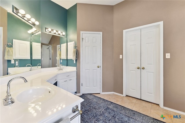 bathroom with a sink, tile patterned flooring, double vanity, baseboards, and walk in shower