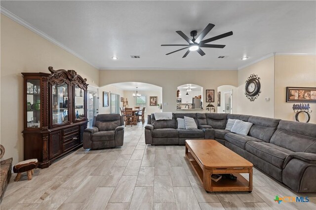 living room with crown molding, arched walkways, ceiling fan with notable chandelier, and visible vents