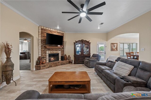living area with crown molding, a ceiling fan, arched walkways, and a fireplace