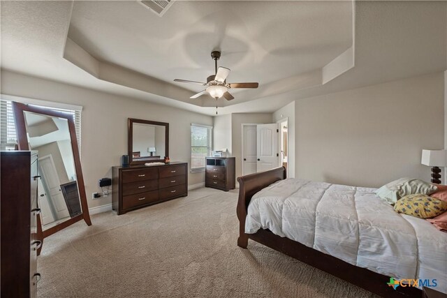 bedroom with ceiling fan, light carpet, a raised ceiling, baseboards, and visible vents