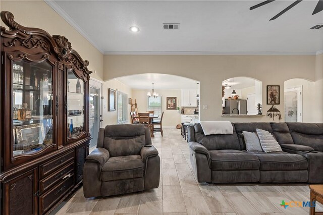 living area with crown molding, arched walkways, ceiling fan with notable chandelier, and visible vents