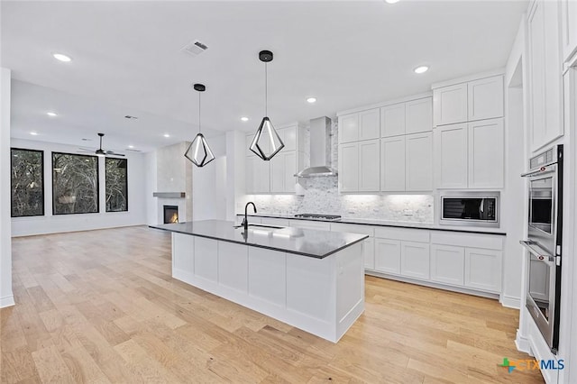 kitchen with wall chimney exhaust hood, hanging light fixtures, a large fireplace, stainless steel appliances, and white cabinets