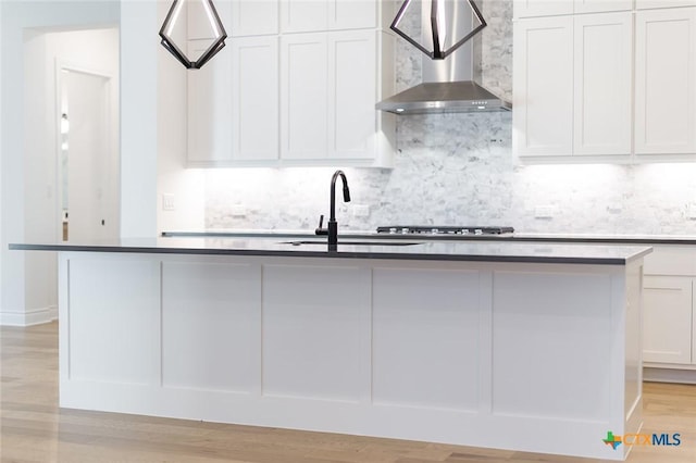 kitchen featuring a kitchen island with sink, white cabinets, and wall chimney exhaust hood