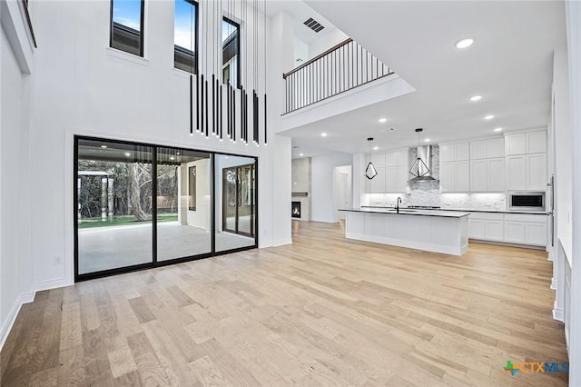 unfurnished living room featuring a towering ceiling, sink, and light hardwood / wood-style flooring