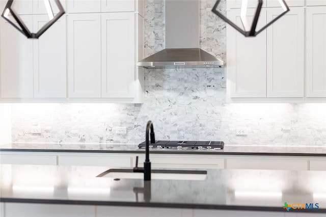 kitchen featuring stainless steel gas stovetop, tasteful backsplash, wall chimney range hood, and white cabinets