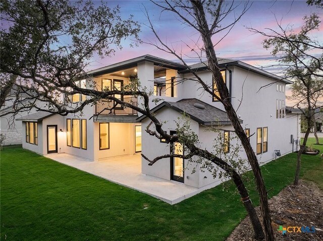 back house at dusk with a lawn and a patio area