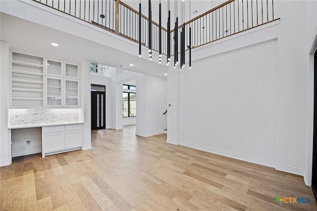 unfurnished living room with a high ceiling, built in desk, and light hardwood / wood-style floors