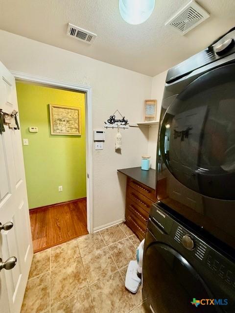 laundry area featuring stacked washer / drying machine, light tile patterned floors, and a textured ceiling