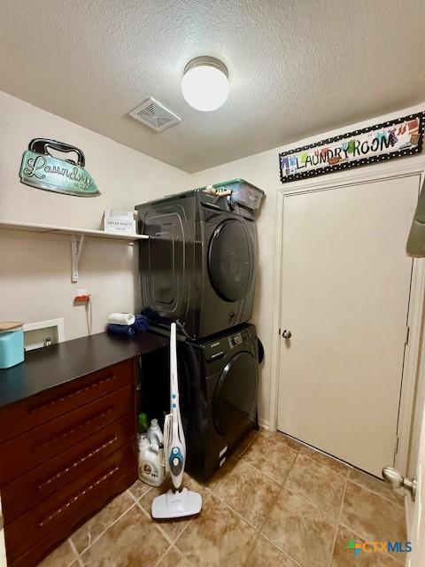 washroom featuring stacked washer / drying machine, light tile patterned floors, and a textured ceiling