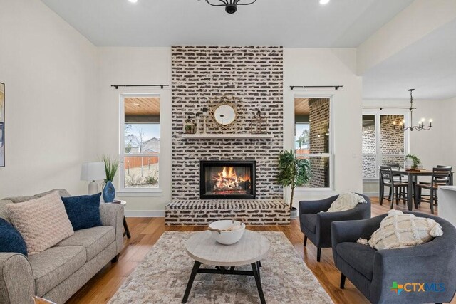 living room with a brick fireplace, light hardwood / wood-style flooring, and an inviting chandelier