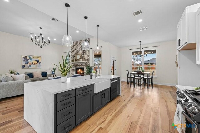 kitchen with hardwood / wood-style flooring, sink, stainless steel dishwasher, light stone countertops, and a fireplace