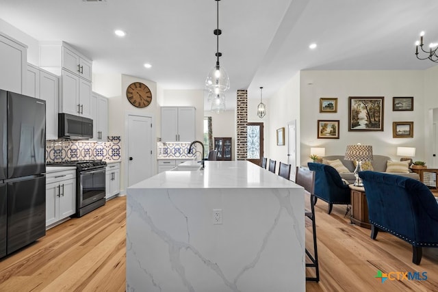 kitchen featuring light hardwood / wood-style flooring, hanging light fixtures, an island with sink, and stainless steel appliances