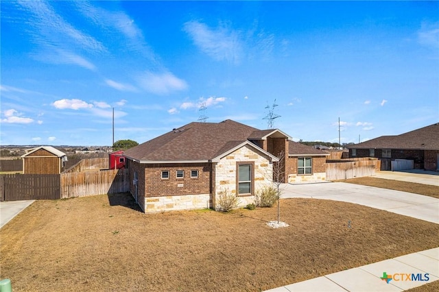 single story home featuring brick siding, roof with shingles, fence, stone siding, and driveway