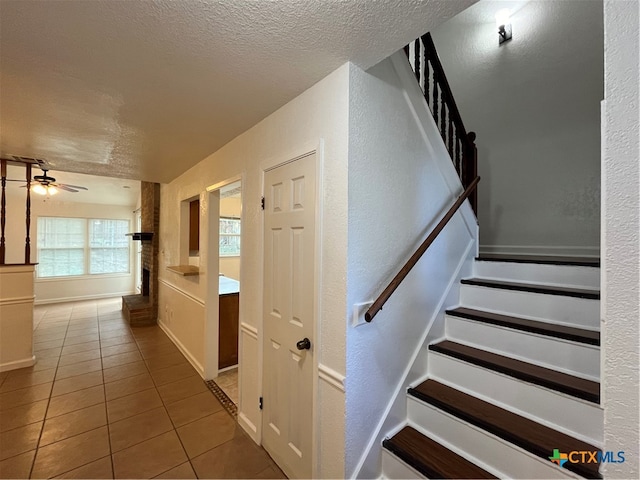 stairs with ceiling fan, tile patterned floors, and a textured ceiling