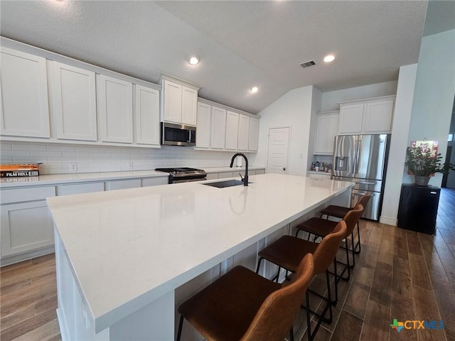 2961 Grove Way, Seguin, TX 78155 - kitchen with stainless steel appliances, tasteful backsplash, a kitchen island with sink, lofted ceiling, and dark wood-style flooring