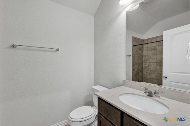 bathroom featuring a tile shower, vanity, toilet, and vaulted ceiling