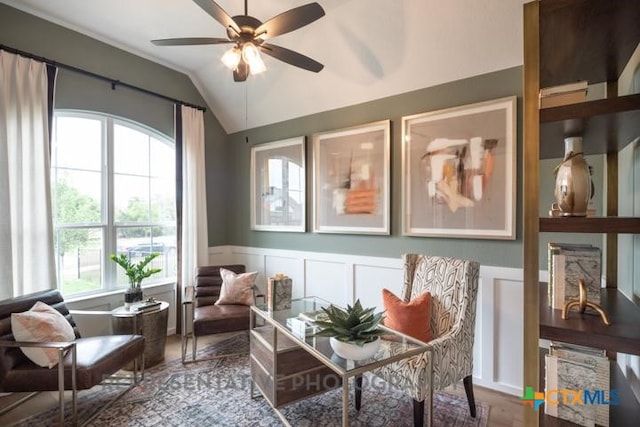 living area with a decorative wall, a wainscoted wall, a ceiling fan, wood finished floors, and lofted ceiling