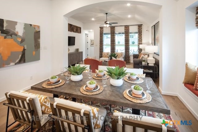 dining space with ceiling fan, arched walkways, vaulted ceiling, wood finished floors, and baseboards