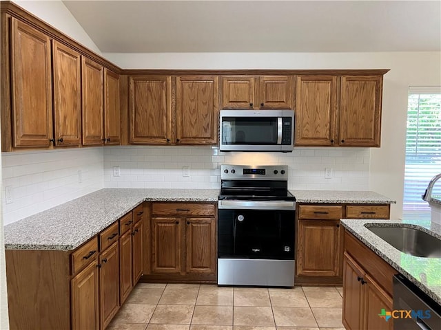512 Constellation Dr, Killeen, TX 76542 - kitchen featuring appliances with stainless steel finishes, brown cabinets, lofted ceiling, light tile patterned flooring, and light stone counters