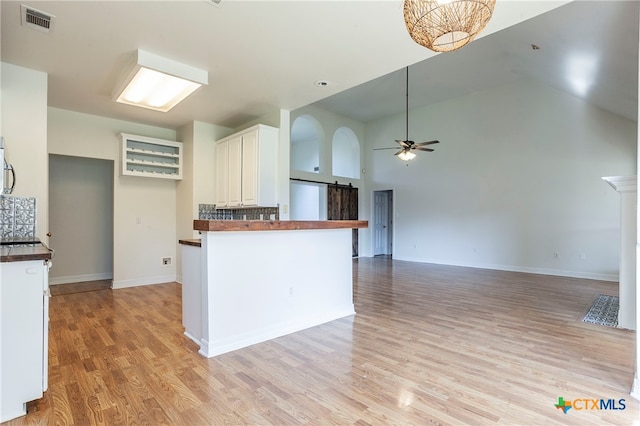 kitchen with white cabinets, kitchen peninsula, high vaulted ceiling, ceiling fan, and light hardwood / wood-style flooring