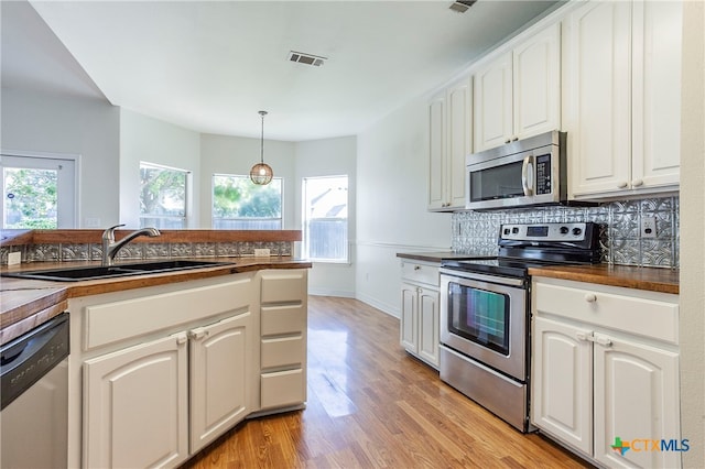 kitchen featuring white cabinetry, sink, appliances with stainless steel finishes, pendant lighting, and light wood-type flooring