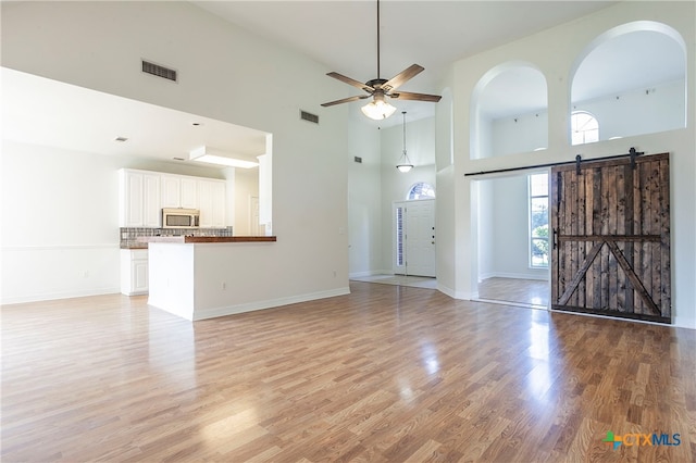 unfurnished living room featuring a towering ceiling, a barn door, and light wood-type flooring