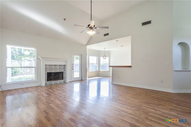 unfurnished living room with high vaulted ceiling, a tiled fireplace, hardwood / wood-style flooring, and ceiling fan