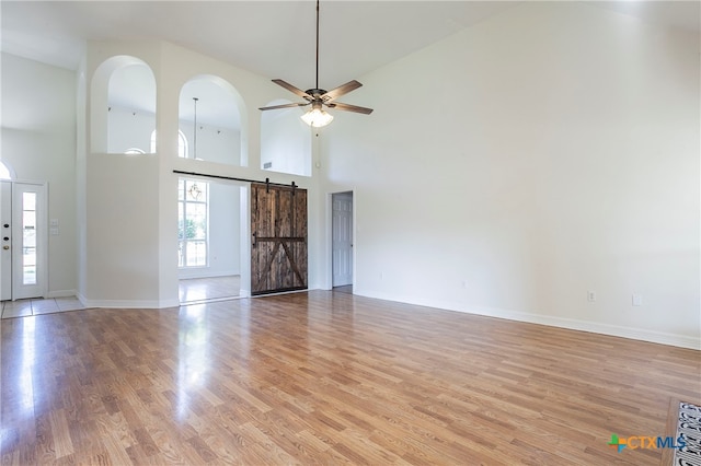 unfurnished living room featuring high vaulted ceiling, light wood-type flooring, a barn door, and ceiling fan