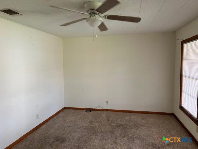 carpeted empty room featuring baseboards, a ceiling fan, and visible vents