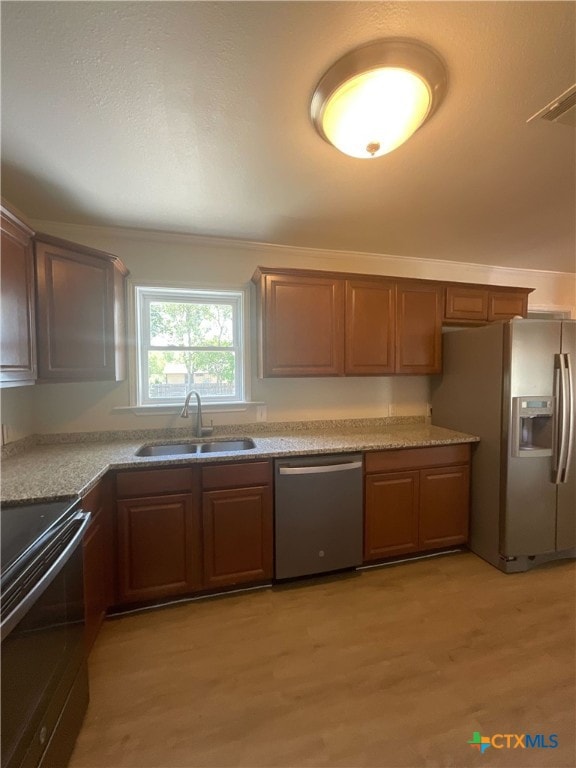 kitchen with appliances with stainless steel finishes, sink, and light hardwood / wood-style flooring