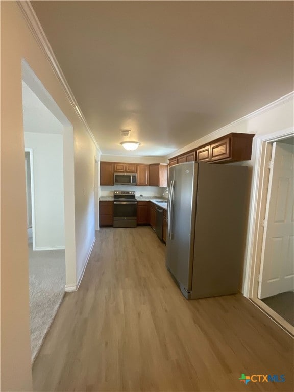 kitchen featuring ornamental molding, appliances with stainless steel finishes, and light hardwood / wood-style flooring