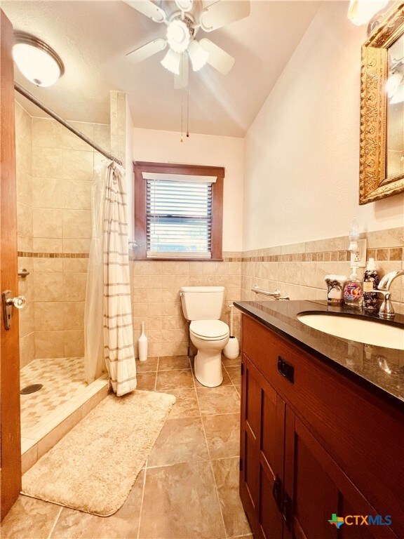 bathroom with a shower with shower curtain, tile walls, ceiling fan, toilet, and vaulted ceiling